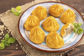 Fried manti dumplings with pepper, basil on brown wooden background and linen textile. Side view,