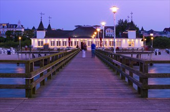 Illuminated pier with strolling people and buildings in the evening light, calm evening mood on the