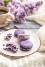 Purple macarons or macaroons cakes with cup of coffee on a gray wooden background and white linen