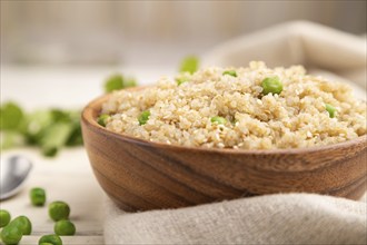 Quinoa porridge with green pea in wooden bowl on a white wooden background and linen textile. Side