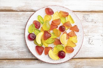 Various fruit jelly candies on plate on white wooden background. top view, flat lay, close up