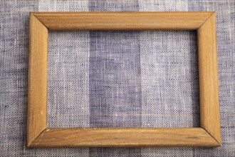 Wooden frame on smooth brown and violet linen tissue. Top view, flat lay, natural textile