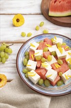 Vegetarian salad with watermelon, feta cheese, and grapes on blue ceramic plate on white wooden