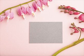 Gray business card with pink dicentra, broken heart flowers on pink pastel background. top view,