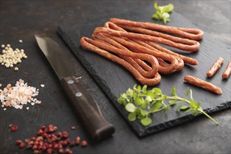 Traditional polish smoked pork sausage kabanos on a slate cutting board with salt and pepper on