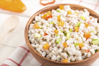 Pearl barley porridge with vegetables in wooden bowl on a white wooden background and linen textile