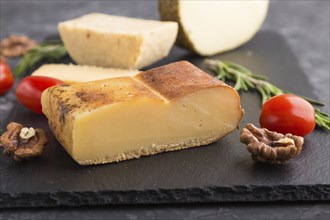 Smoked cheese and various types of cheese with rosemary and tomatoes on black slate board on a