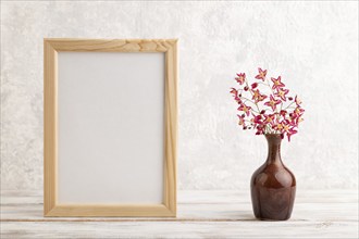 Wooden frame with purple barrenwort flowers in ceramic vase on gray concrete background. side view,