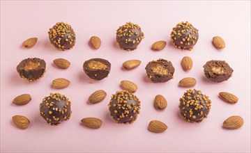 Chocolate caramel ball candies with almonds in a row on a pastel pink background. side view, close