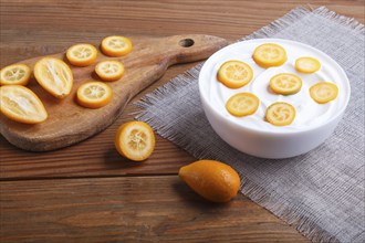 Greek yogurt with kumquat pieces in a white plate on a brown wooden background, close up