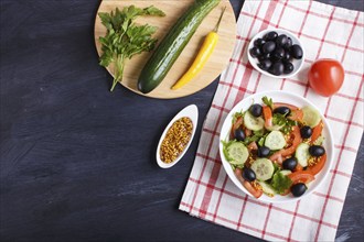 Vegetarian salad of tomatoes, cucumbers, parsley, olives and mustard on linen tablecloth and black