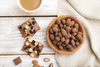 Almond in chocolate dragees in wooden plate and a cup of coffee on white wooden background and