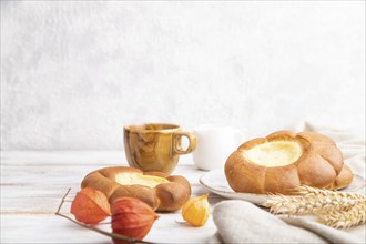 Sour cream bun with cup of coffee on a white wooden and concrete background and linen textile. Side