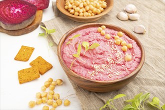 Hummus with beet and microgreen basil sprouts in wooden bowl on a white wooden background and linen