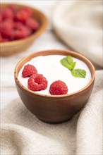 Yogurt with raspberry in clay cups on white wooden background and linen textile. Side view, close