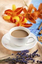 Orange day-lily and lavender flowers and a cup of coffee on a blue concrete background, with orange