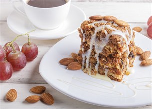 Pie with caramel, white milk sauce and almonds on a white plate on a white wooden background. close