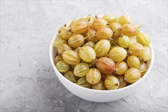 Fresh green gooseberry in white bowl on gray concrete background. side view, close up