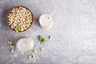 Organic non dairy cashew milk in glass and wooden plate with cashew nuts on a gray concrete