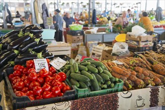 Colourful display of vegetables at a market stall with price tags and background activity, market