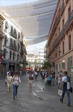 Fabric spread over buildings to provide shade in busy shopping street in central Seville, Spain,