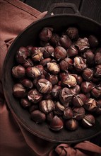 Roasted chestnuts, in an iron pan, wooden table, top view, no people, rustic style