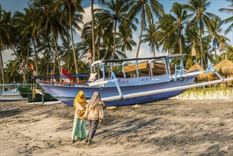 Muslim woman in the evening sun at Mangsit beach in Sengiggi, boat, fishing boat, palm beach,