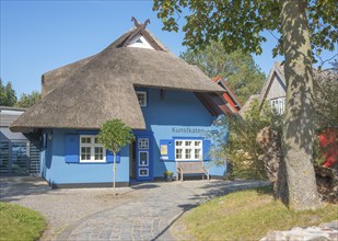 A picturesque, blue-painted thatched roof house with bench in front of the entrance, open door,