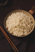 A plate of boiled rice, with wooden sticks, on a brown background, no people, selective focus,