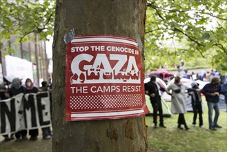 Poster Stop the genocide in Gaza / The camps resist on a tree in front of a human chain at the