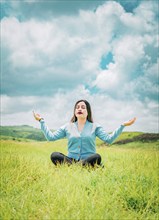 Portrait of relaxed young woman doing yoga in a field. Beautiful girl meditating on the grass in a