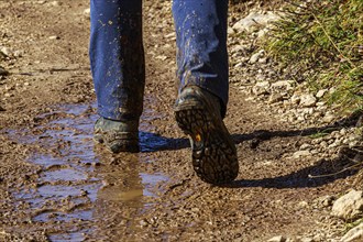 A person in hiking boots on a muddy path outdoors