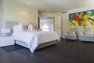 Master bedroom with queen size bed, white lacquered nightstands, upholstered armchairs and dark