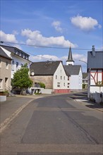 Street with houses under a blue sky with cumulus clouds in Beuren, Eifel, district of Cochem-Zell,