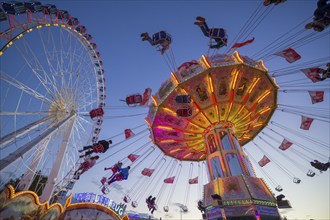 A funfair at dusk with illuminated chain carousel and Ferris wheel, Europa Rad, rides, wave flight,