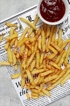 Fried French fries, scattered on a newspaper, with red sauce, top view, no people