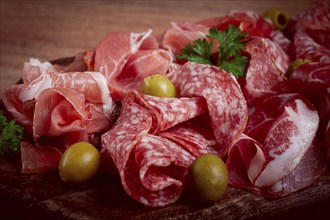 Assortment, sliced meat appetizer, prosciutto, salami and ham, with olives, on a wooden board,