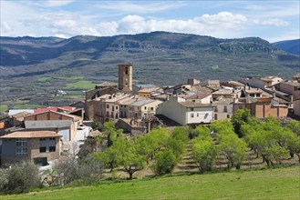 A picturesque village with a clock tower in a mountainous landscape under a clear blue sky, Guardia