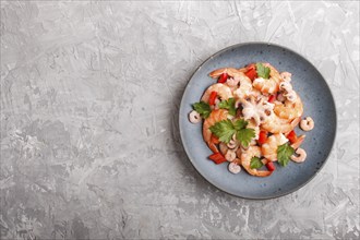 Boiled shrimps or prawns and small octopuses with herbs on a blue ceramic plate on a gray concrete