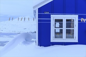 Typical Greenlandic house in deep snow in front of mountains, winter, Tasiilaq, East Greenland,