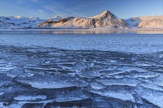 Ice floes on a lake in front of snowy mountains, sun, evening light, snow, winter, Snaefellsnes,