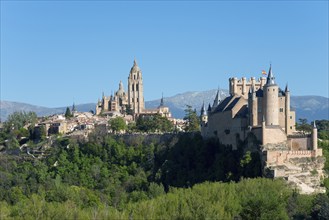 Medieval city with castle and cathedral, surrounded by trees and mountains in sunny weather,