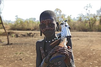 South Ethiopia, in Maco National Park, Mursi tribe, Mursi boy with painted face and rifle,