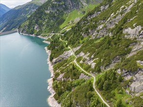 The shoreline of a reservoir with a road winding along the mountains, under a cloudy sky, Klein