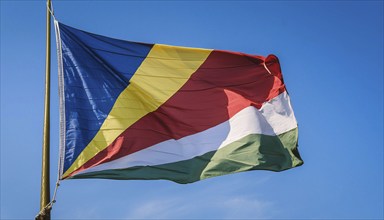 The flag of Seychelles, fluttering in the wind, isolated against a blue sky