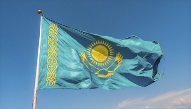 The flag of Kazakhstan flutters in the wind, isolated against a blue sky