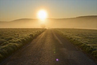 Sunrise over a misty hilly landscape with green meadow and trees in a peaceful atmosphere,