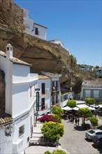 Whitewashed houses nestled in rocks, a charming terrace with trees under a clear blue sky, cave