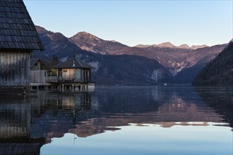 Lake Grundlsee in autumn at sunset. Boathouses on the left, mountains in the background. Blue sky,