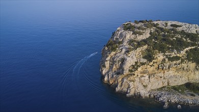 Drone shot, boat sailing along a rocky cliff over the clear blue sea, Anthony Quinn Bay, Vagies